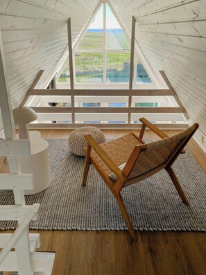 Ein Zimmer mit hohen Decken und einem großen Oberlicht, ein Holzstuhl, ein weißer Stuhl und ein gestrickter Teppich.