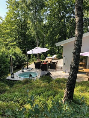 A wooden deck with outdoor furniture, a hot tub, and a patio umbrella. - Modern stone house with hot tub in Åsljunga forest (Örkelljunga)