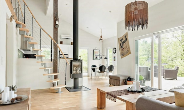 A modern interior with a spiral staircase, a fireplace, and a dining area with outdoor views. - Modern stone house with hot tub in Åsljunga forest (Örkelljunga)