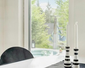 A view through a window of a pool area with a chair, candles, and a house in the background. - Modern stone house with hot tub in Åsljunga forest (Örkelljunga)
