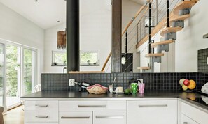 A modern kitchen with white cabinets, a black countertop, and a wooden staircase. - Modern stone house with hot tub in Åsljunga forest (Örkelljunga)