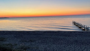 Ein Strand mit einem hölzernen Steg, der sich in ruhiges Wasser bis zum Sonnenuntergang erstreckt.