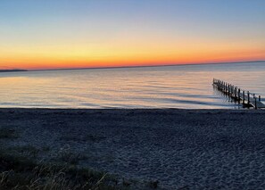 Ein Strand mit einem hölzernen Steg, der sich in ruhiges Wasser bis zum Sonnenuntergang erstreckt.