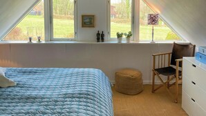 Ein Schlafzimmer mit Bett, Stuhl, Kommode und Fenster mit Blick ins Freie.