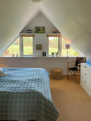 Ein Schlafzimmer mit Bett, Stuhl, Kommode und Fenster mit Blick ins Freie.
