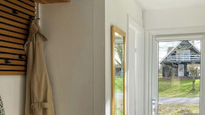 Ein Zimmer mit einer Holzbank, einem Kleiderständer, einem Spiegel und einer zur Außenseite führenden Tür.