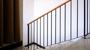 A staircase with a wooden handrail and black metal balusters, leading to a landing with a light fixture. - 3-bedroom apartment in Downtown San José (San José)