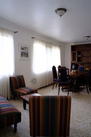 Un salon avec des fauteuils à rayures, une table à manger avec des chaises, un ventilateur de plafond et un tableau encadré au mur.
