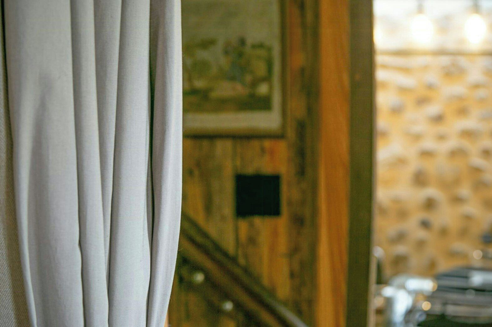 A room with a wooden wall, a framed picture, and a window with curtains.