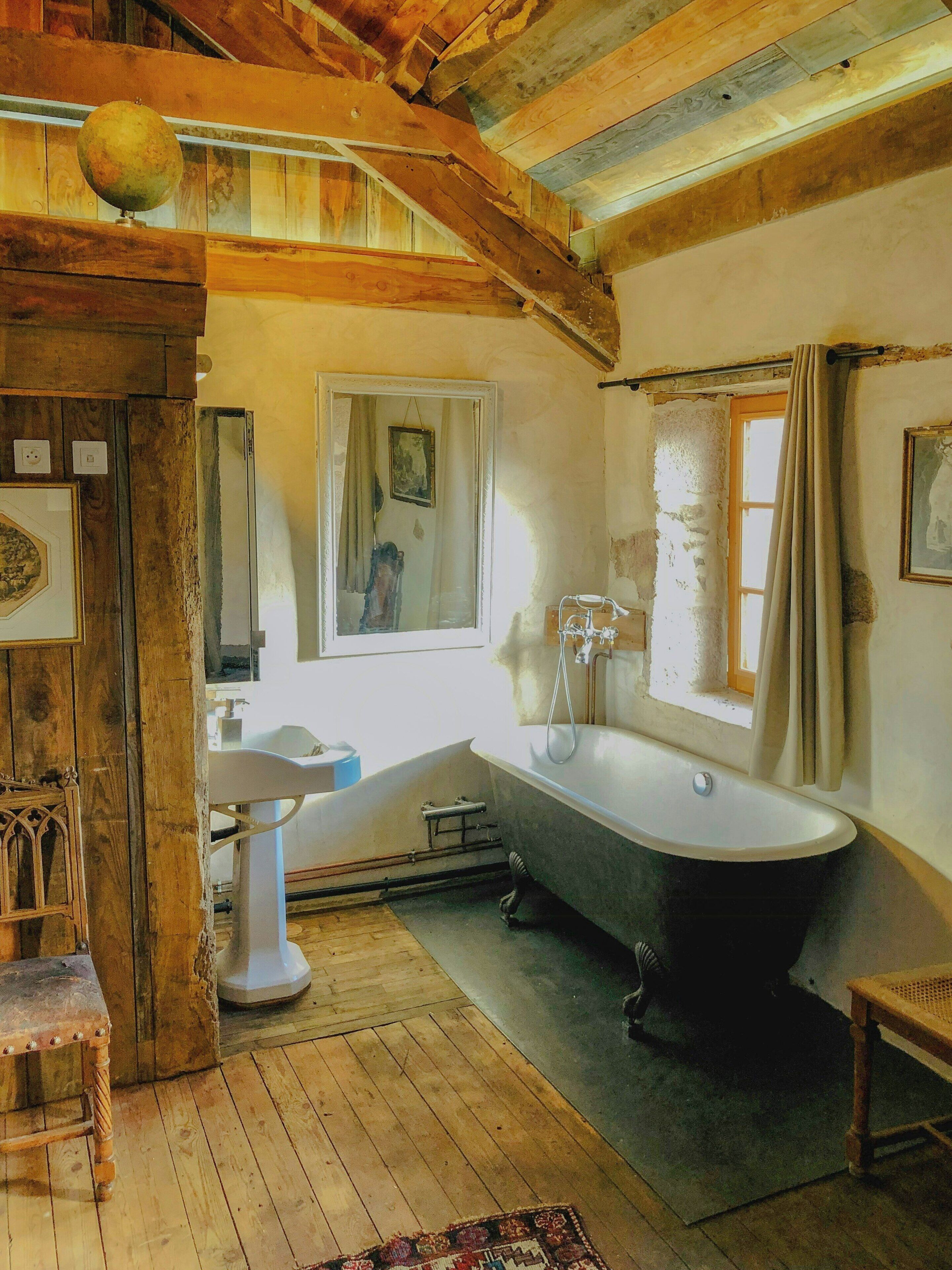 A rustic bathroom with a freestanding bathtub, a pedestal sink, and wooden beams on the ceiling.