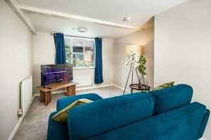 Ein Wohnzimmer mit einem blauen Sofa, einem Fernseher, einer Lampe und einem Fenster mit Vorhängen.