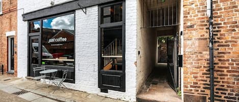 A coffee shop with a white facade, black-framed windows, and a visible outdoor seating area with tables and chairs.