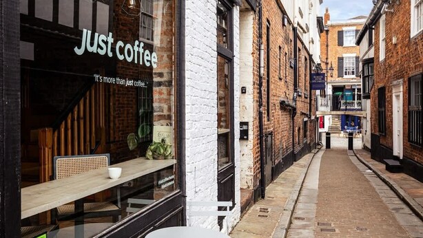 A narrow street with a café named 'Just Coffee' on the left, featuring a wooden bench outside. - Central Chester Recently Renovated 1BR Flat (Chester)
