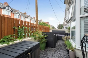 Un espacio exterior reducido con cerramiento de madera, plantas en macetas y mobiliario de exterior.