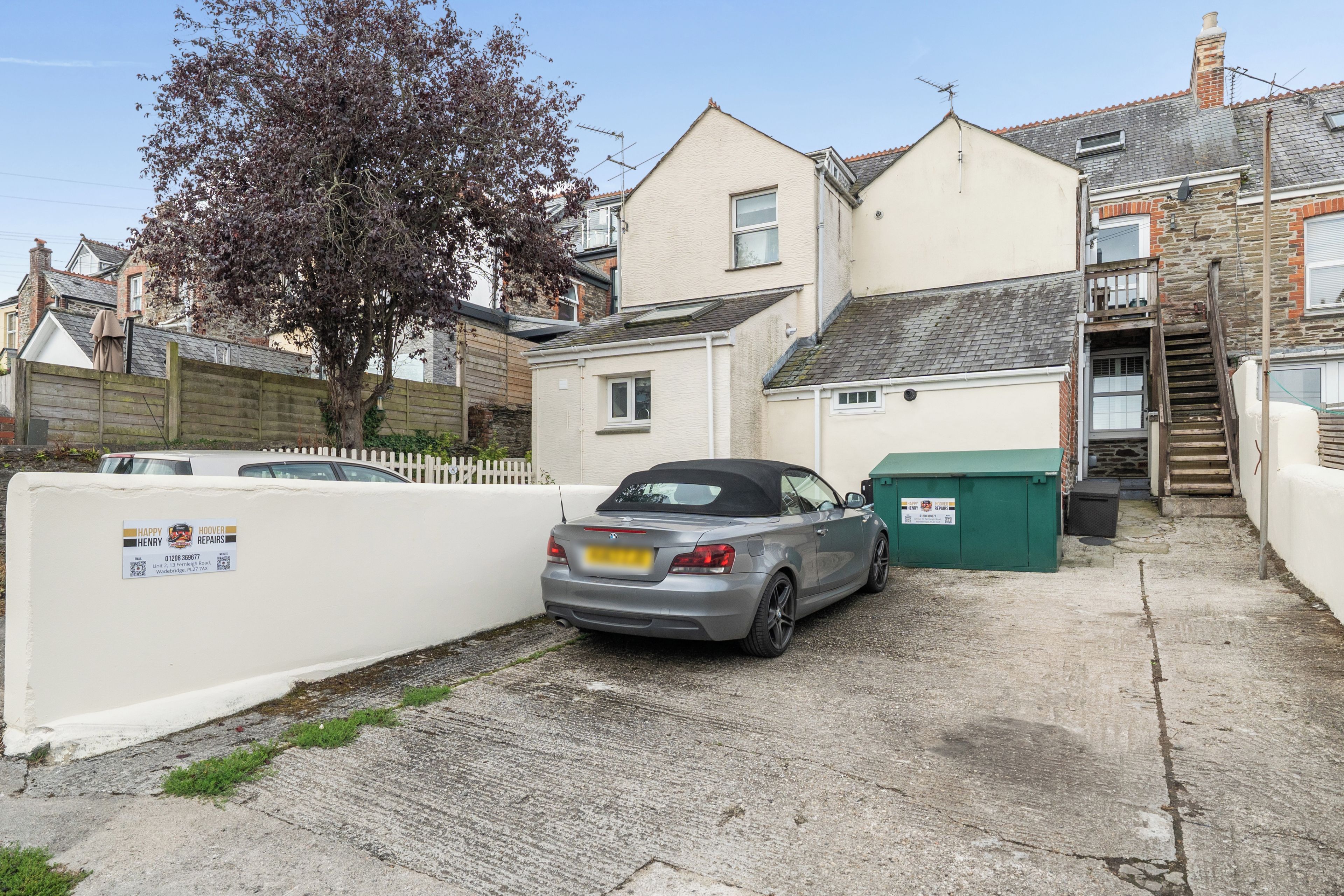 A residential street with a parked car, a white fence, and a tree.