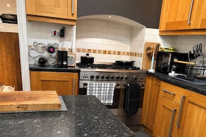 A kitchen with wooden cabinets, a stove, oven, and a microwave. - 1 Bed - Sleeps 4 - Parking - Pets - Town Centre (Wadebridge)