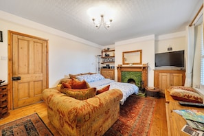 A cozy room with a bed, a sofa, a television, and a fireplace. - 1 Bed - Sleeps 4 - Parking - Pets - Town Centre (Wadebridge)