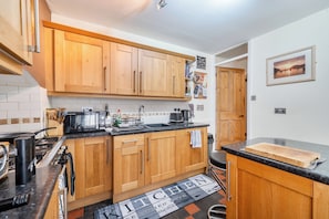 A kitchen with wooden cabinets, a black countertop, a coffee maker, and a black and white patterned doormat.