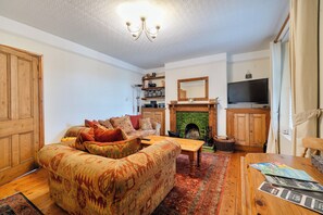 A living room with a sofa, a fireplace, a television, and wooden cabinets. - 1 Bed - Sleeps 4 - Parking - Pets - Town Centre (Wadebridge)