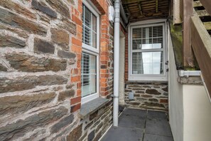 Un muro de piedra con una ventana y una puerta, una tubería blanca y un suelo de piedra.