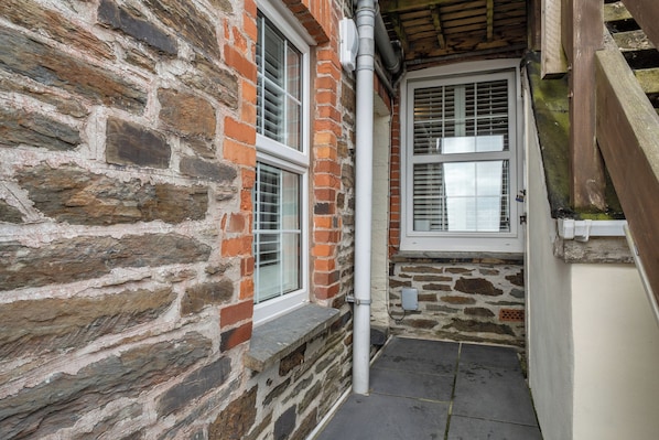 A stone wall with a window and a door, a white pipe, and a stone floor.