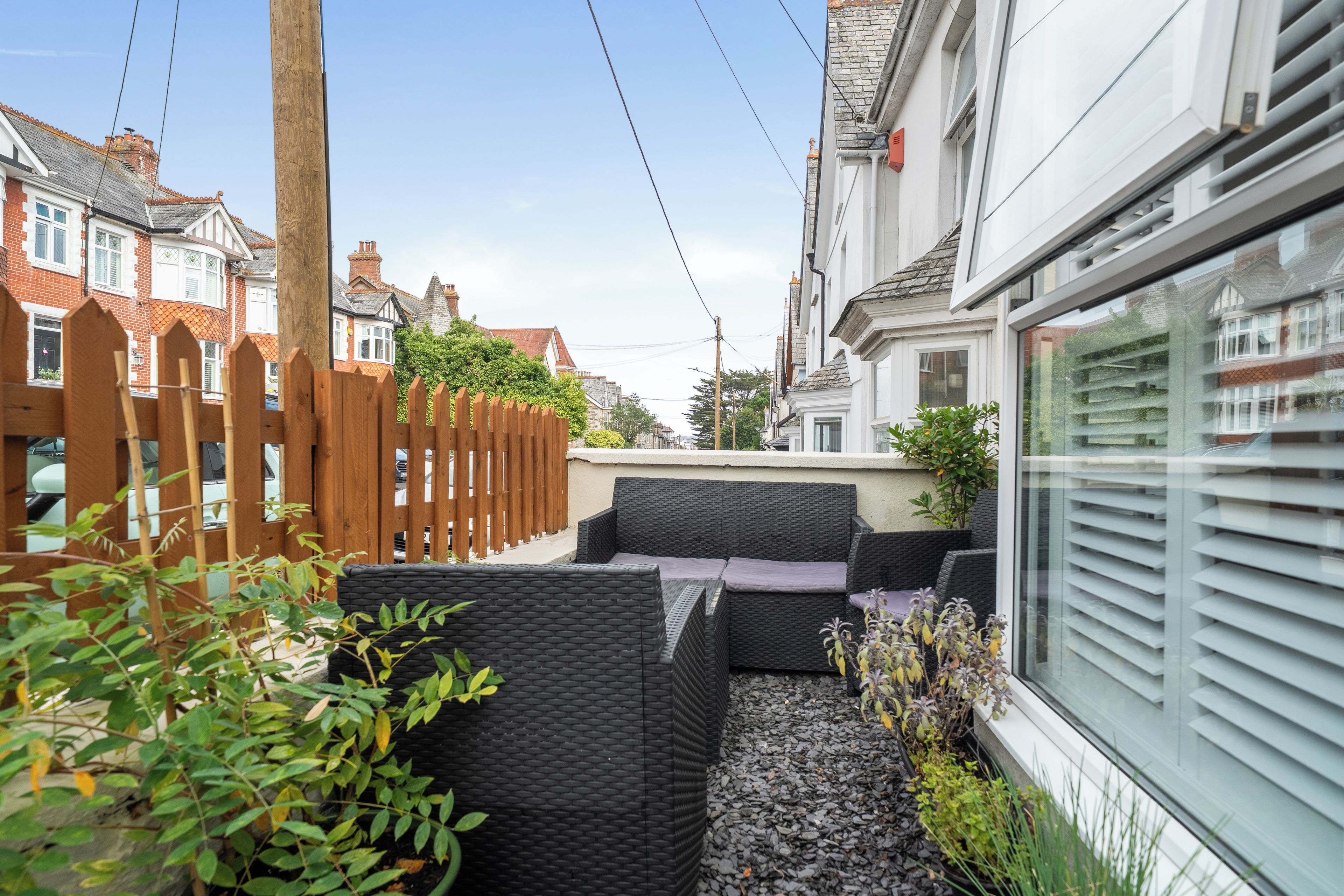 A narrow urban street with traditional houses, a wooden fence, and a seating area with wicker furniture.