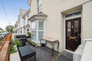 A residential property with a front garden, a wooden fence, a black table, and a dark brown door.