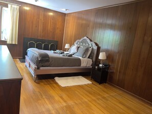 Une chambre avec un grand lit, deux tables de chevet, une commode et un plancher en bois.