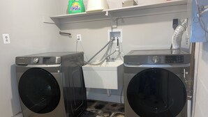 A laundry room with two front-loading washing machines, a sink, and a shelf with cleaning supplies. - Amazing 6-bedroom house with AC in adorable Bethesda (Bethesda)