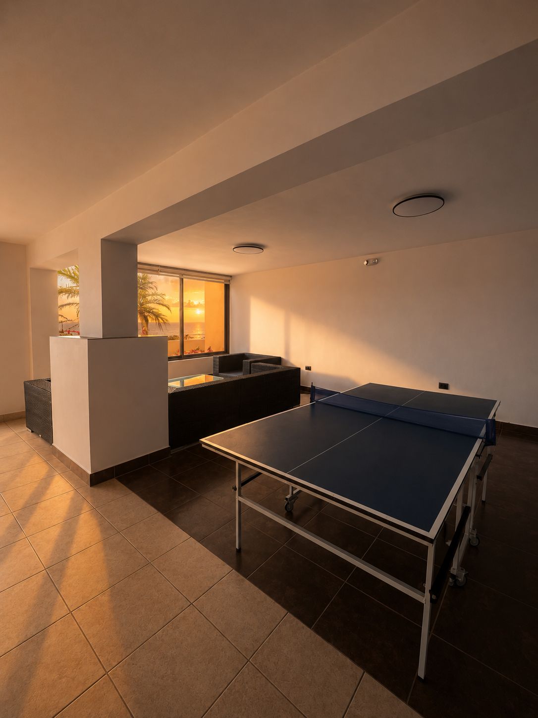 A room with a ping pong table, a seating area, and a window with a view.
