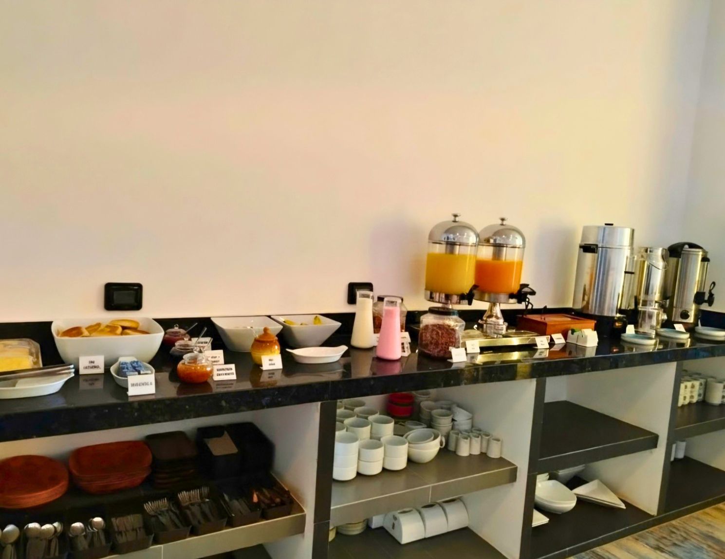 A buffet setup with various food items and beverages, including a juice dispenser and a coffee machine.