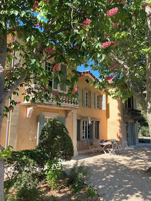 A building with a balcony, a small garden area with a table and chairs, and a tree with pink flowers. - 17th century estate near Aix-en-Provence (Aix-en-Provence)