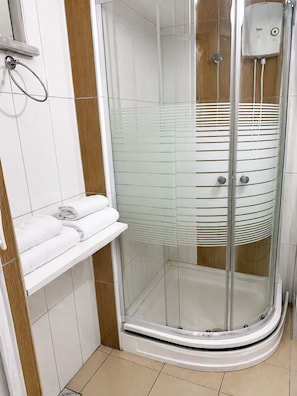 Eine gläserne Dusche mit weiß gefliesten Wänden, einem Handtuchhalter und einem Warmwasserbereiter.