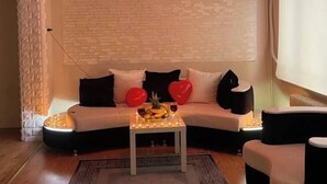 A living room with a white sofa, red heart-shaped pillows, a small table with candles, and a decorative hanging light. - green yeşil otel (Bursa)