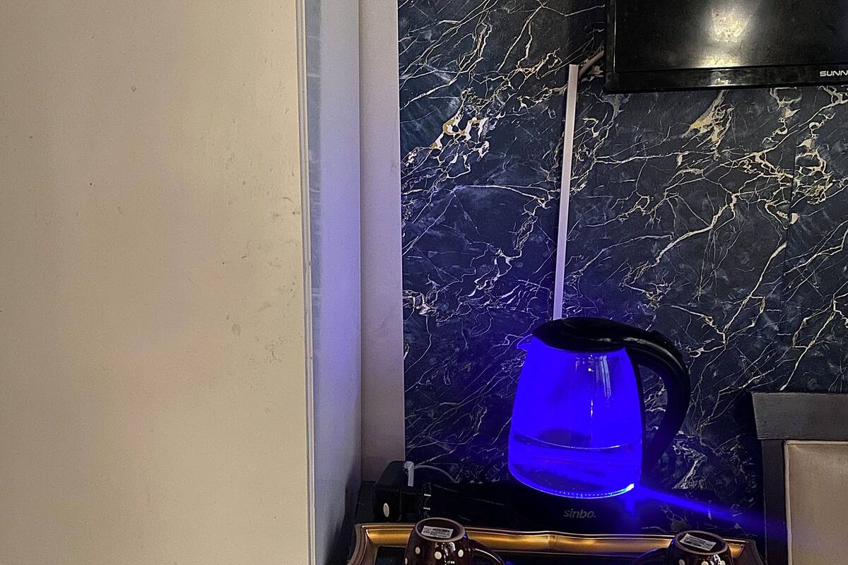 A kitchen area with a marble backsplash, a coffee maker, and a tray with two mugs and a box of Nescafé instant coffee.
