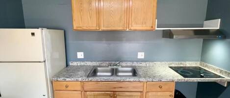 A compact kitchen with wooden cabinets, a built-in sink, a stove, and a refrigerator.