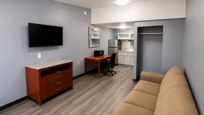 Sala moderna com televisão de tela plana, móveis de madeira, um sofá e uma cozinha compacta ao fundo.