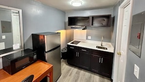 Uma cozinha compacta com micro-ondas, geladeira, pia e armários escuros.