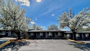 Fileira de quartos de motel com estacionamento na frente, árvores e céu limpo.