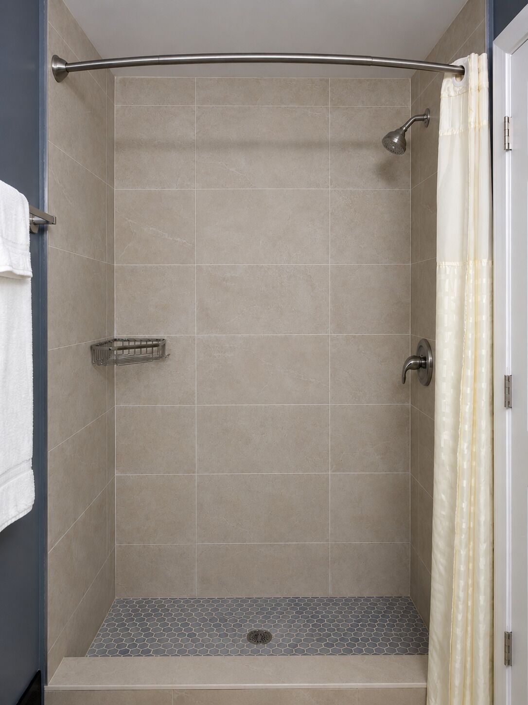 Ducha con barra metálica curva, paredes y suelo de azulejos.