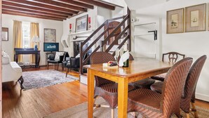 Een eetruimte met een houten tafel, rieten stoelen, een piano en een trap.
