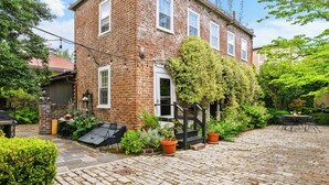 Een bakstenen huis met een tuin, een terras met tafel en stoelen, en een klein zitgedeelte buiten.