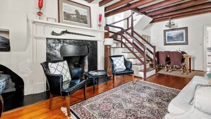 Een woonkamer met een open haard, twee leren fauteuils, een kamerbreed tapijt, houten balken en een trap.