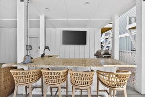 A kitchen with a large island, wicker bar stools, a flat-screen TV, and a grill. - Summer Open! 1 Min Walk to Beach, Pool & Spa (Ocean Isle Beach)