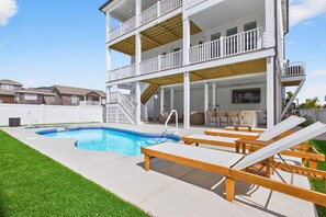 Une maison à deux étages avec une piscine, des chaises longues et un patio couvert.