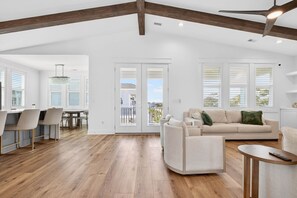 Un vaste espace de vie doté d’un plancher en bois, d’un canapé, d’une table à manger avec des chaises et de grandes fenêtres équipées de stores.