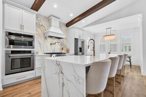 A modern kitchen with marble countertops, stainless steel appliances, and a central island with bar stools. - Summer Open! 1 Min Walk to Beach, Pool & Spa (Ocean Isle Beach)