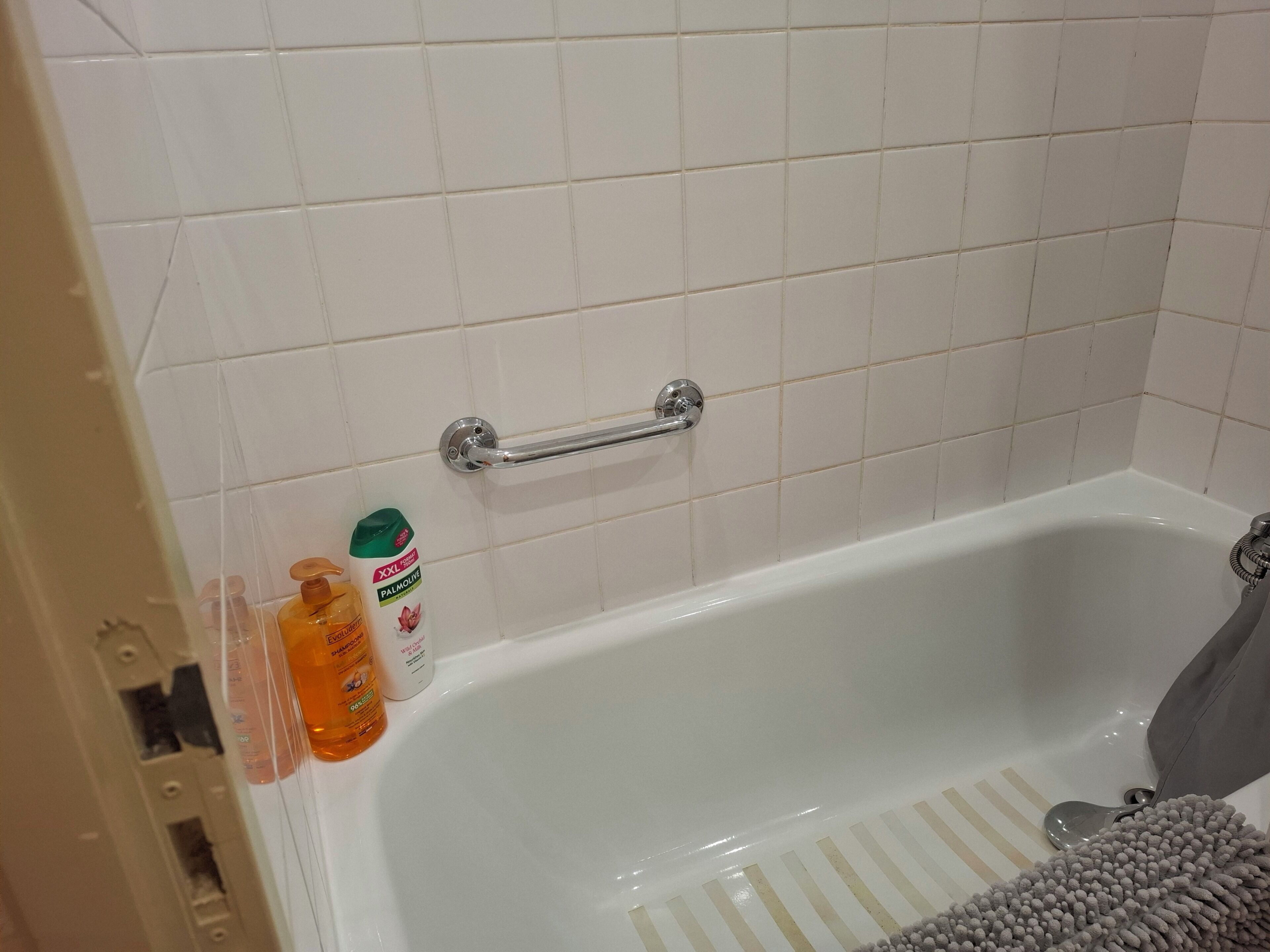 Een badkuip met een greep, een badmat met strepen en twee flessen toiletartikelen.