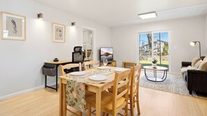 Ein modernes Wohnzimmer mit Essbereich, Fernseher und einem großen Fenster mit Blick ins Freie.