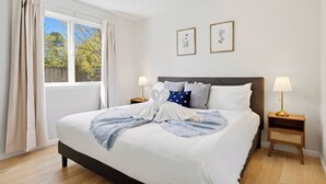 Ein ordentlich bezogenes Bett mit einer blauen Decke, zwei Nachttischlampen und zwei gerahmten Pflanzenbildern an der Wand.